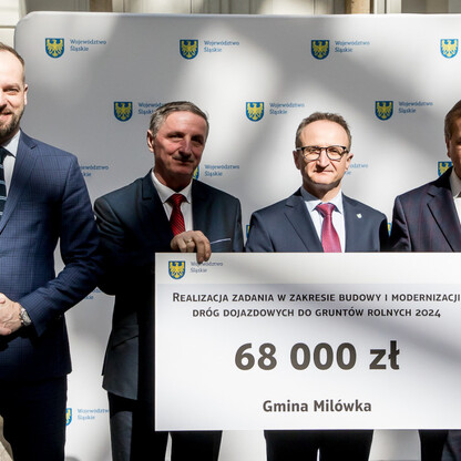 Grzegorz Boski, wicemarszałek województwa, prezentuje symboliczny czek na modernizację dróg dojazdowych do gruntów rolnych w Gminie Milówka. (wygenerowano przez AI)