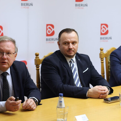 Trzy osoby w garniturach uczestniczą w konferencji prasowej w Bieruniu, omawiając modernizację drogi wojewódzkiej. (wygenerowano przez AI)