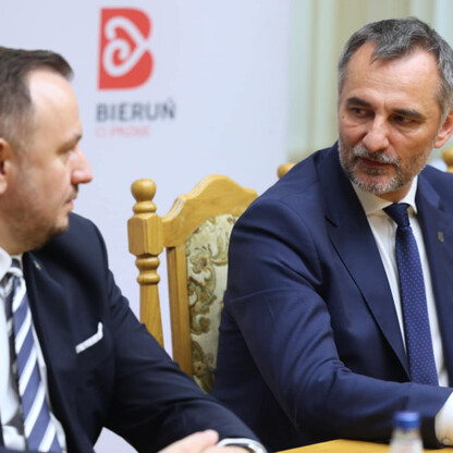Dwóch mężczyzn w strojach formalnych siedzi przy stole, dyskutując o budowie drogi w Bieruniu. (wygenerowano przez AI)